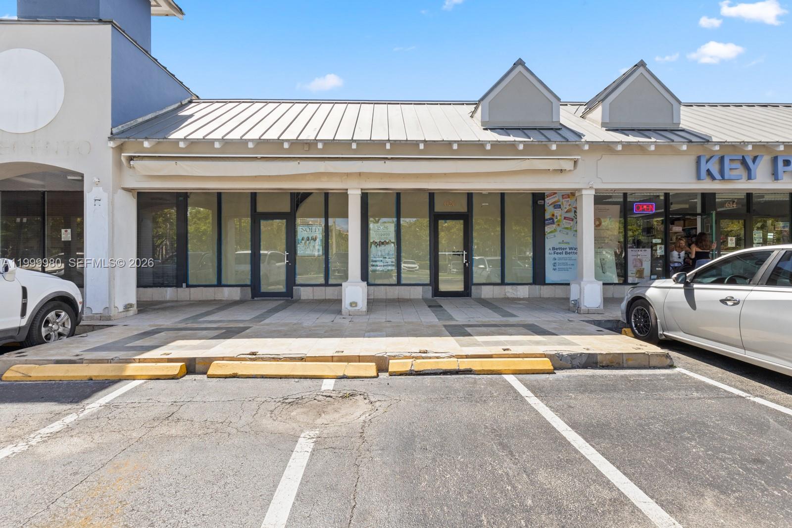 A commercial storefront with a metal roof and glass doors sits behind a parking lot — 620 Crandon Blvd # 7, Key Biscayne FL 33149, KEY BISCAYNE, FL