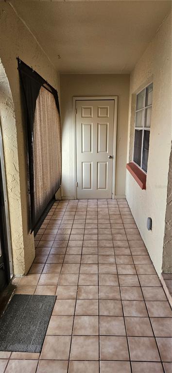 A covered entryway with light-colored tile flooring, a white door, and a window with shutters — 6468 BONNIE BAY CIRCLE N UNIT 0, PINELLAS PARK, FL