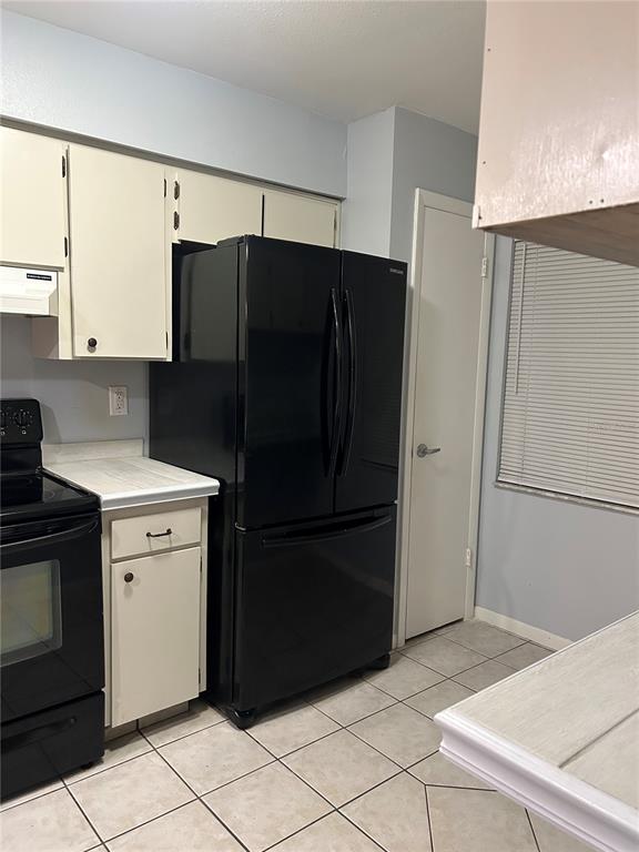 A kitchen features white cabinets, black appliances, and light-colored tile flooring — 6468 BONNIE BAY CIRCLE N UNIT 0, PINELLAS PARK, FL
