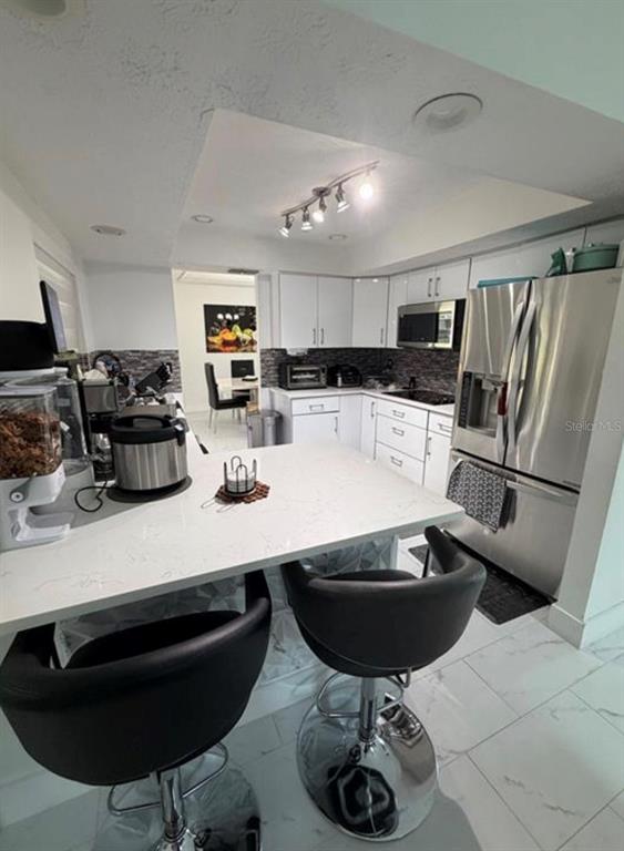 A modern kitchen features white cabinets, stainless steel appliances, and a breakfast bar with stools — 209 SW 42ND STREET, CAPE CORAL, FL