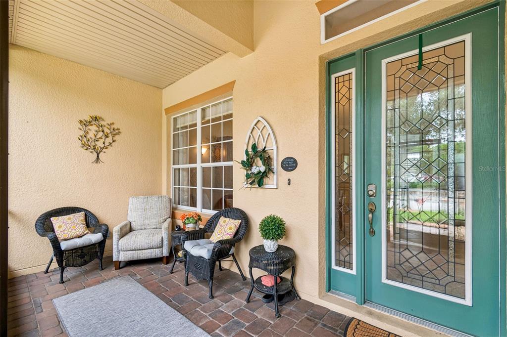 A covered front porch features brick pavers, wicker seating, and a green glass-paneled front door — 600 VOLTERRA BOULEVARD, POINCIANA, FL
