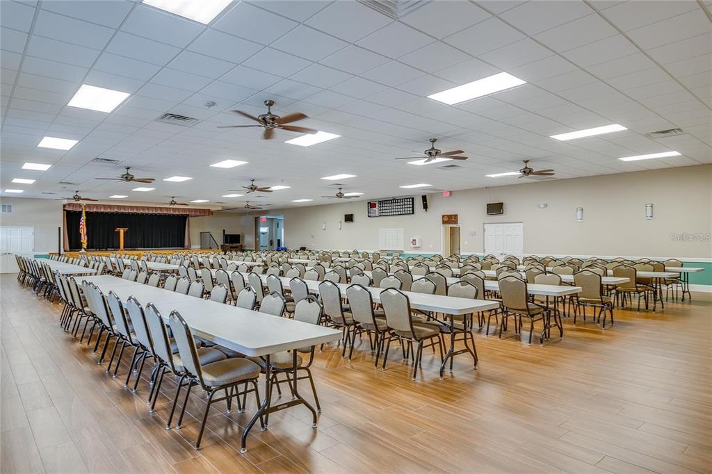 A large, open event hall features rows of tables and chairs, a stage, and ceiling fans — 5976 CORMORANT COURT, LAKELAND, FL