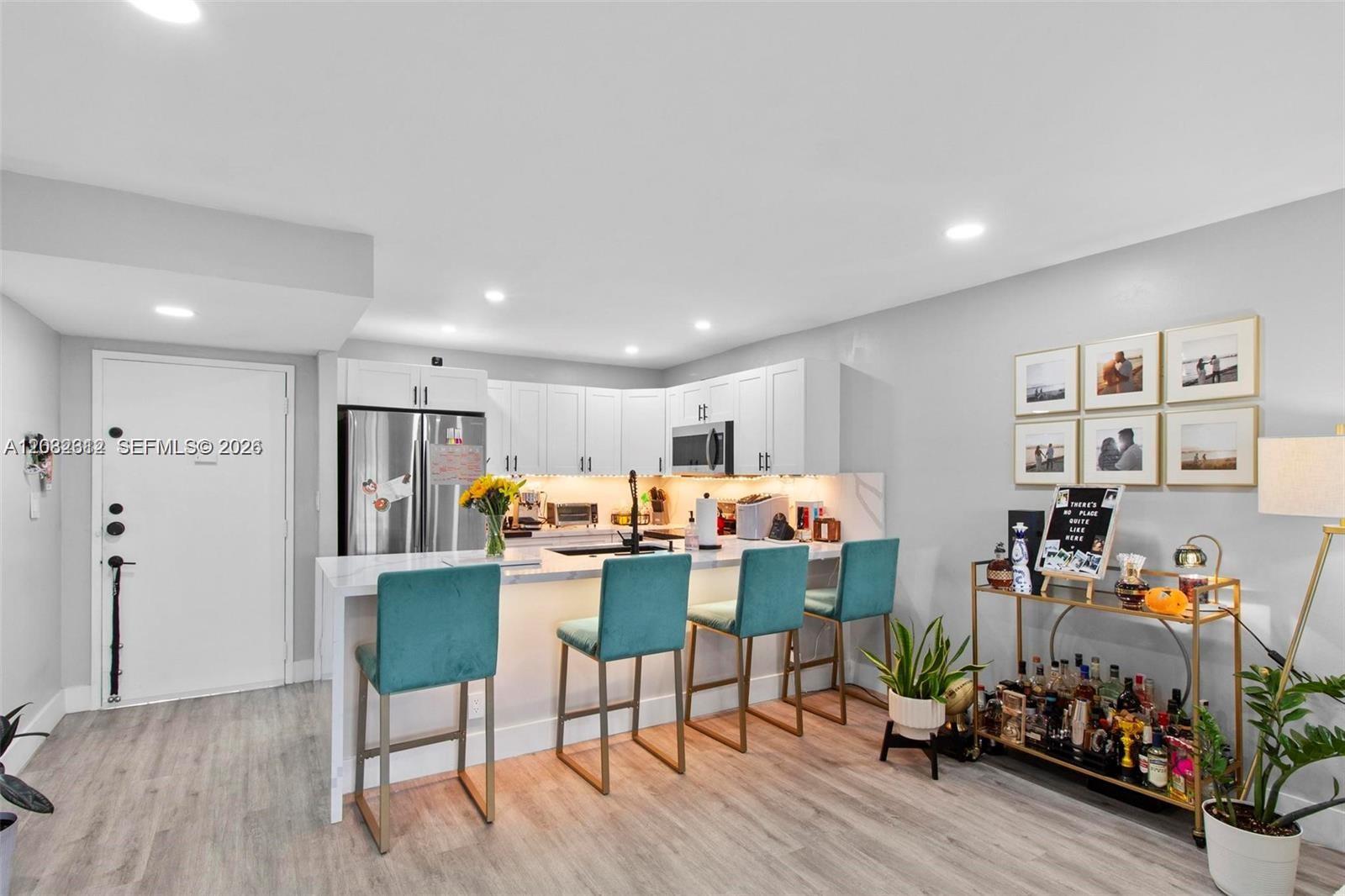 A kitchen features white cabinetry, a marble-topped island with four teal barstools, and light flooring — 7725 SW 86th St # 420, Miami FL 33143, MIAMI, FL
