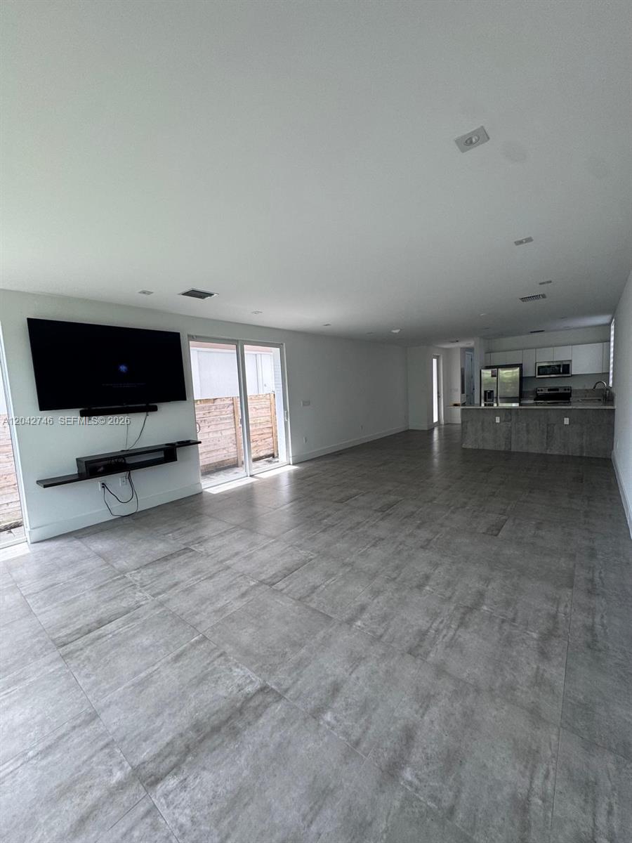 An open-concept living area features large gray floor tiles, a wall-mounted television, and a kitchen — 2947 SW 27th Ter # 0, Miami FL 33133, MIAMI, FL