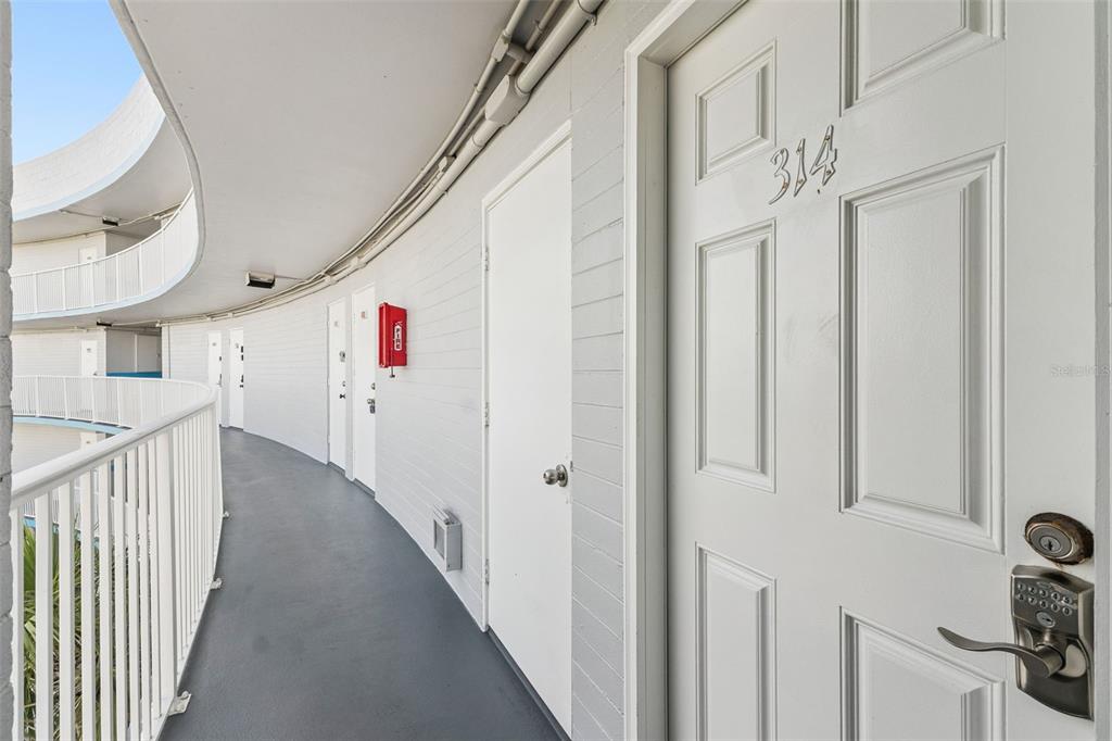 A curved outdoor walkway leads past several white doors, including one marked 314 — 1233 S ATLANTIC AVENUE UNIT 3140, DAYTONA BEACH, FL