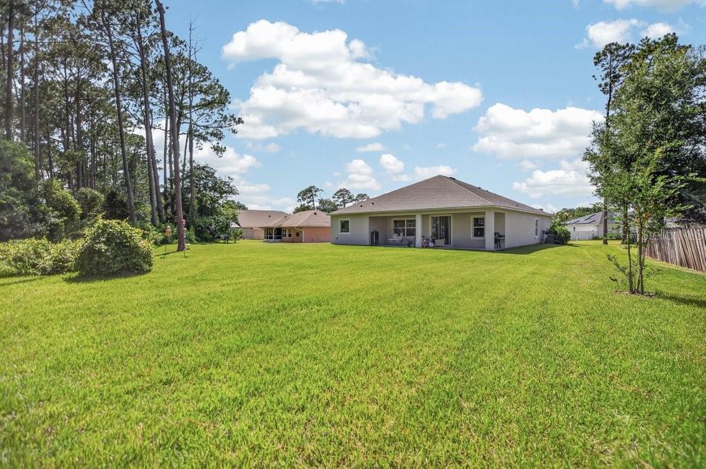 A large, grassy backyard features a single-story house with a covered patio and tall trees — 14 WOODWORTH DRIVE, PALM COAST, FL