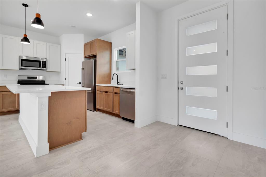A modern kitchen features wood-toned cabinetry, white countertops, stainless steel appliances, and a glass-paneled door — 6168 SW 154TH STREET, OCALA, FL