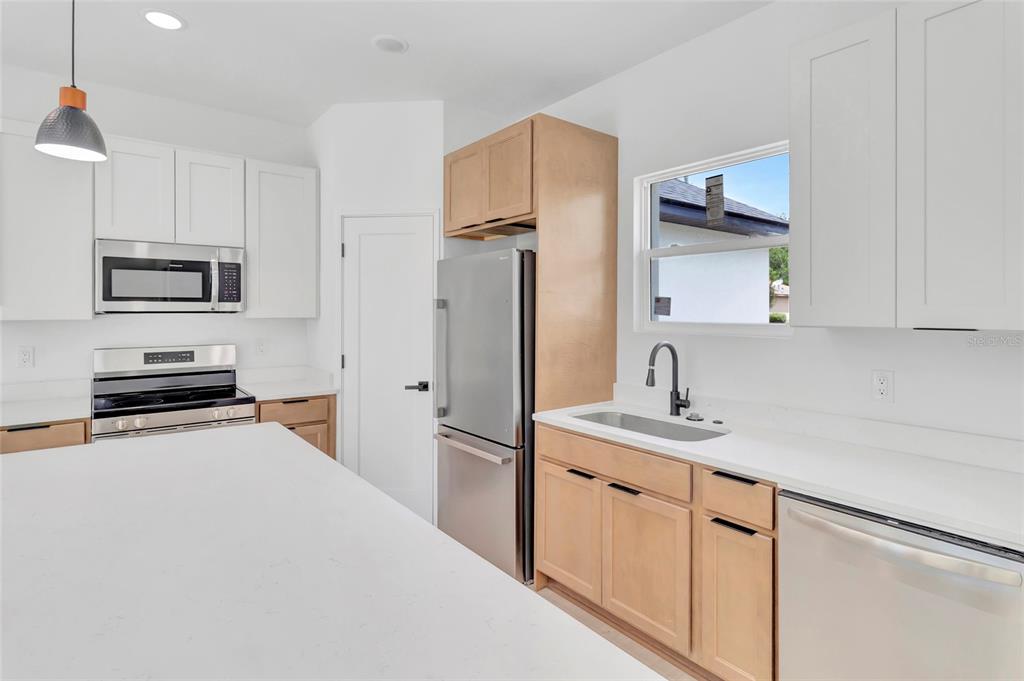 A kitchen features white upper cabinets, light wood lower cabinets, stainless steel appliances, and countertops — 6168 SW 154TH STREET, OCALA, FL