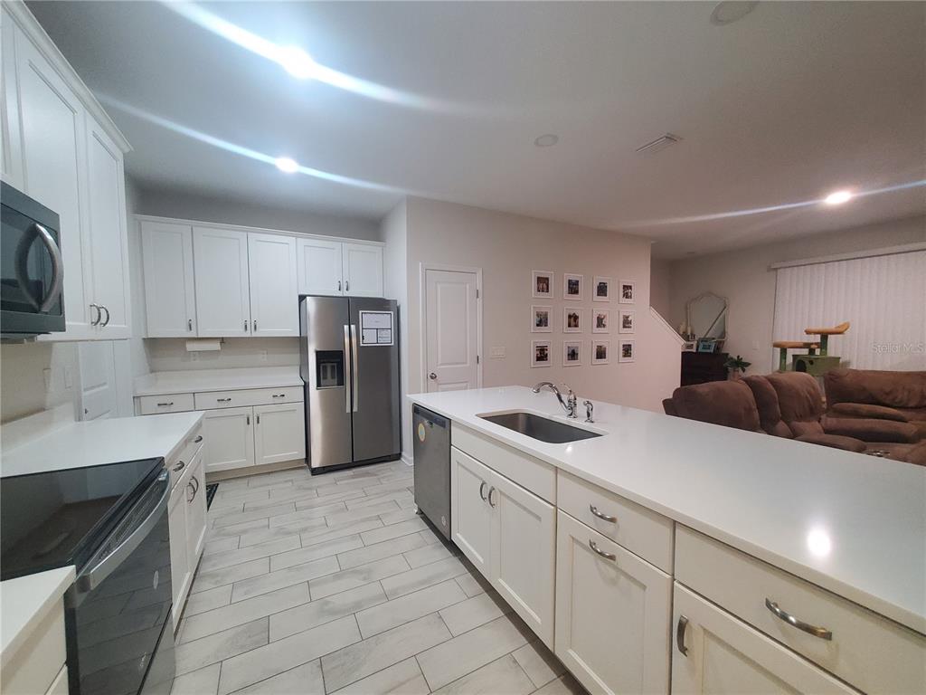 A modern kitchen features white cabinets, stainless steel appliances, and a large central island — 10960 BRIGHTLEAF COURT, RIVERVIEW, FL