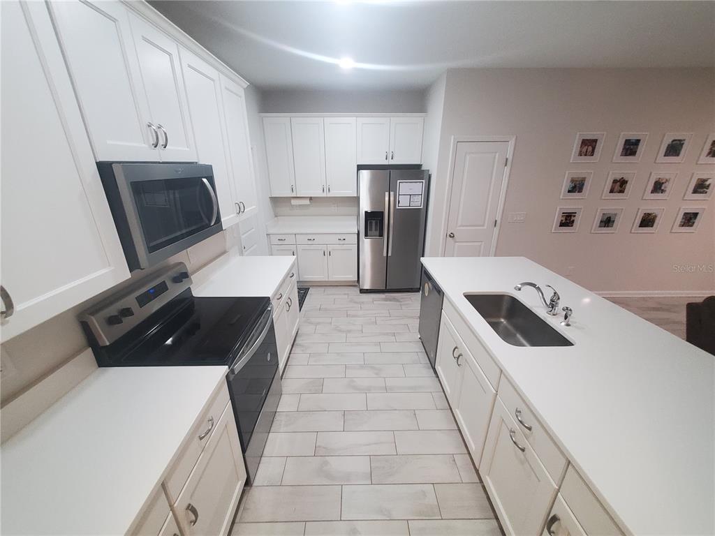 A kitchen features white cabinets, stainless steel appliances, a center island, and light-colored tile flooring — 10960 BRIGHTLEAF COURT, RIVERVIEW, FL