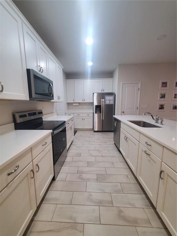 A kitchen features white cabinets, stainless steel appliances, quartz countertops, and light-colored tile flooring — 10960 BRIGHTLEAF COURT, RIVERVIEW, FL