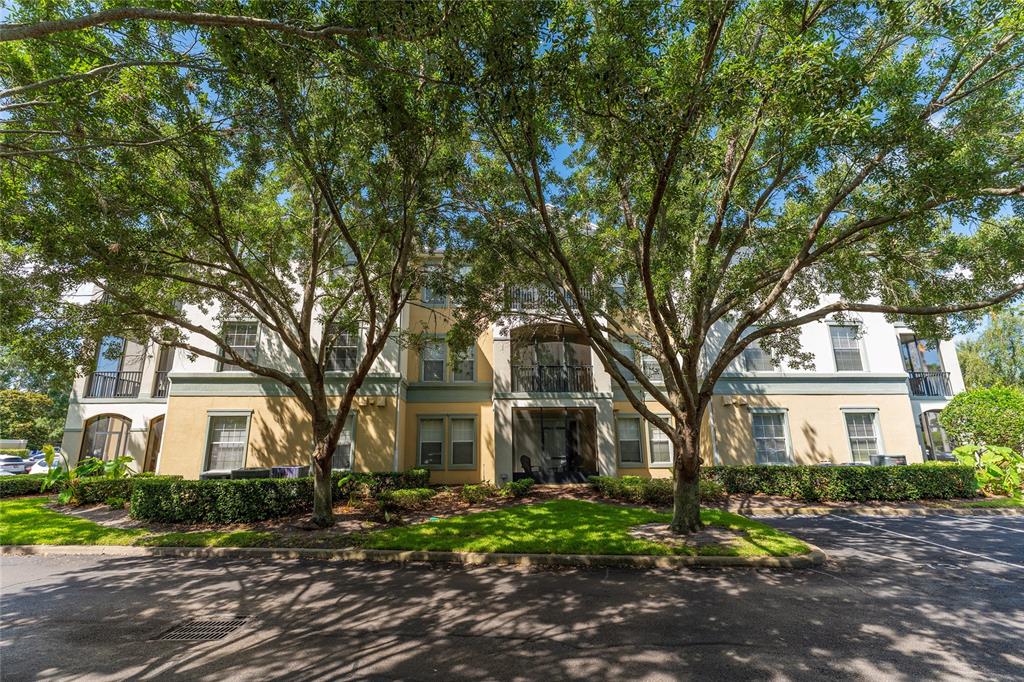 A three-story apartment building with tan stucco walls and large trees in the foreground — 8180 BOAT HOOK LOOP UNIT 109, WINDERMERE, FL