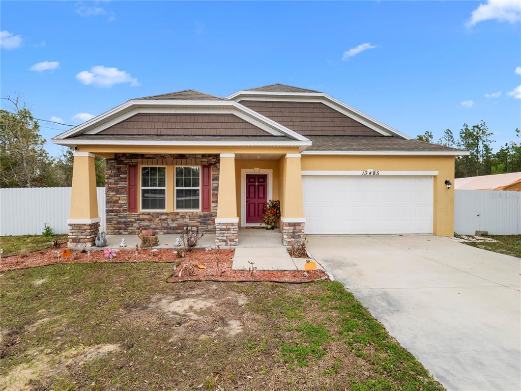 A single-story house with a tan stucco exterior, stone accents, and a two-car garage — 13485 RESORT AVENUE, BROOKSVILLE, FL