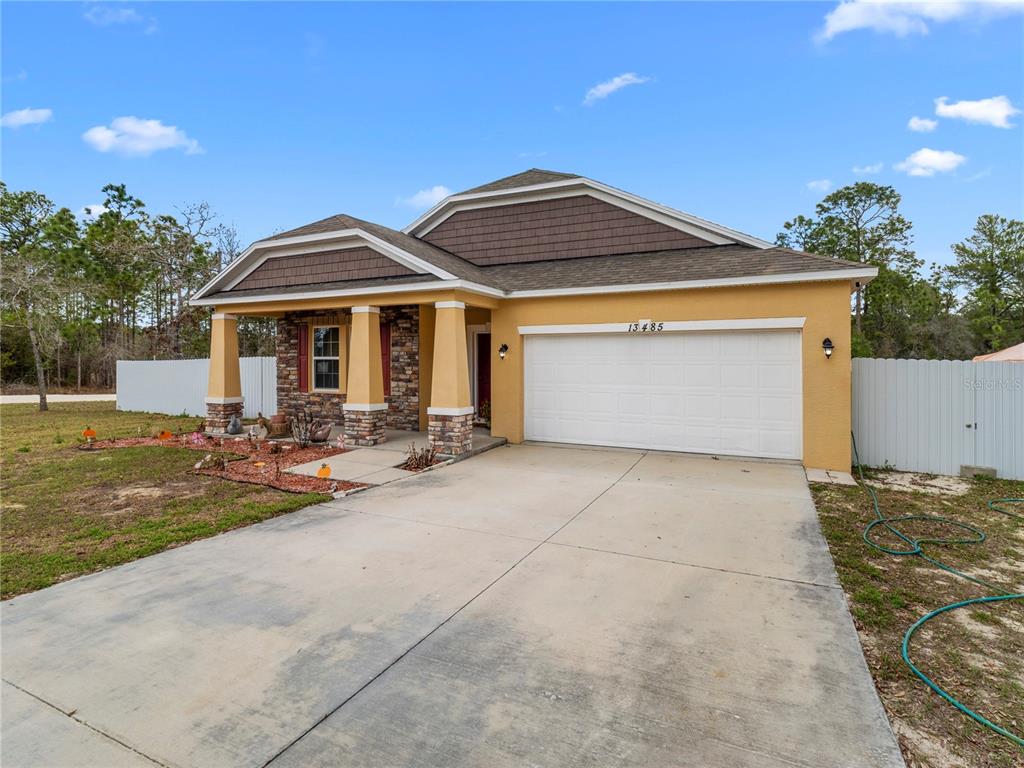A single-story house with a tan stucco exterior, stone accents, and a two-car garage — 13485 RESORT AVENUE, BROOKSVILLE, FL