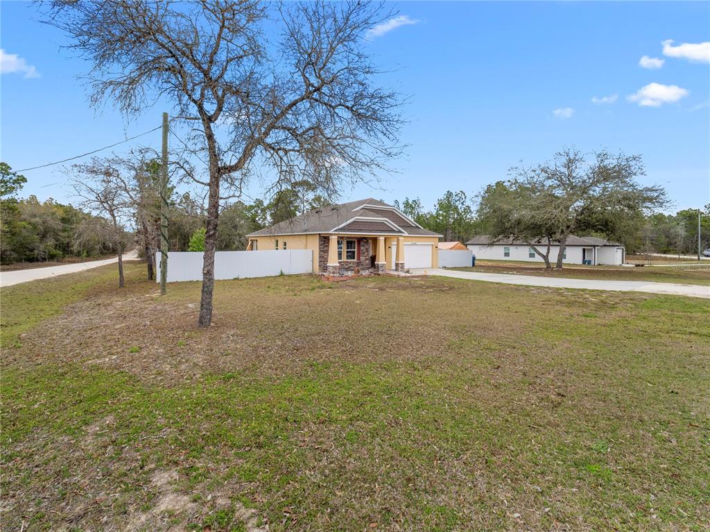 A tan single-story house with a stone facade and white fence sits on a grassy lot — 13485 RESORT AVENUE, BROOKSVILLE, FL