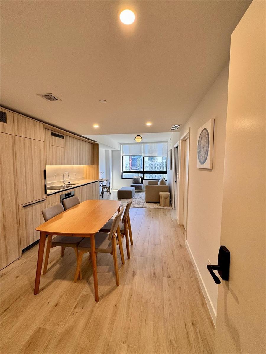 A modern apartment features a kitchen with light wood cabinetry, a dining table, and living area — 225 N Miami Avenue # 2507, Miami FL 33128, MIAMI, FL