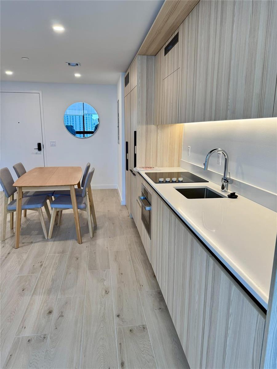 A modern kitchen with light wood cabinetry, white countertops, and an adjacent dining area — 225 N Miami Avenue # 2507, Miami FL 33128, MIAMI, FL