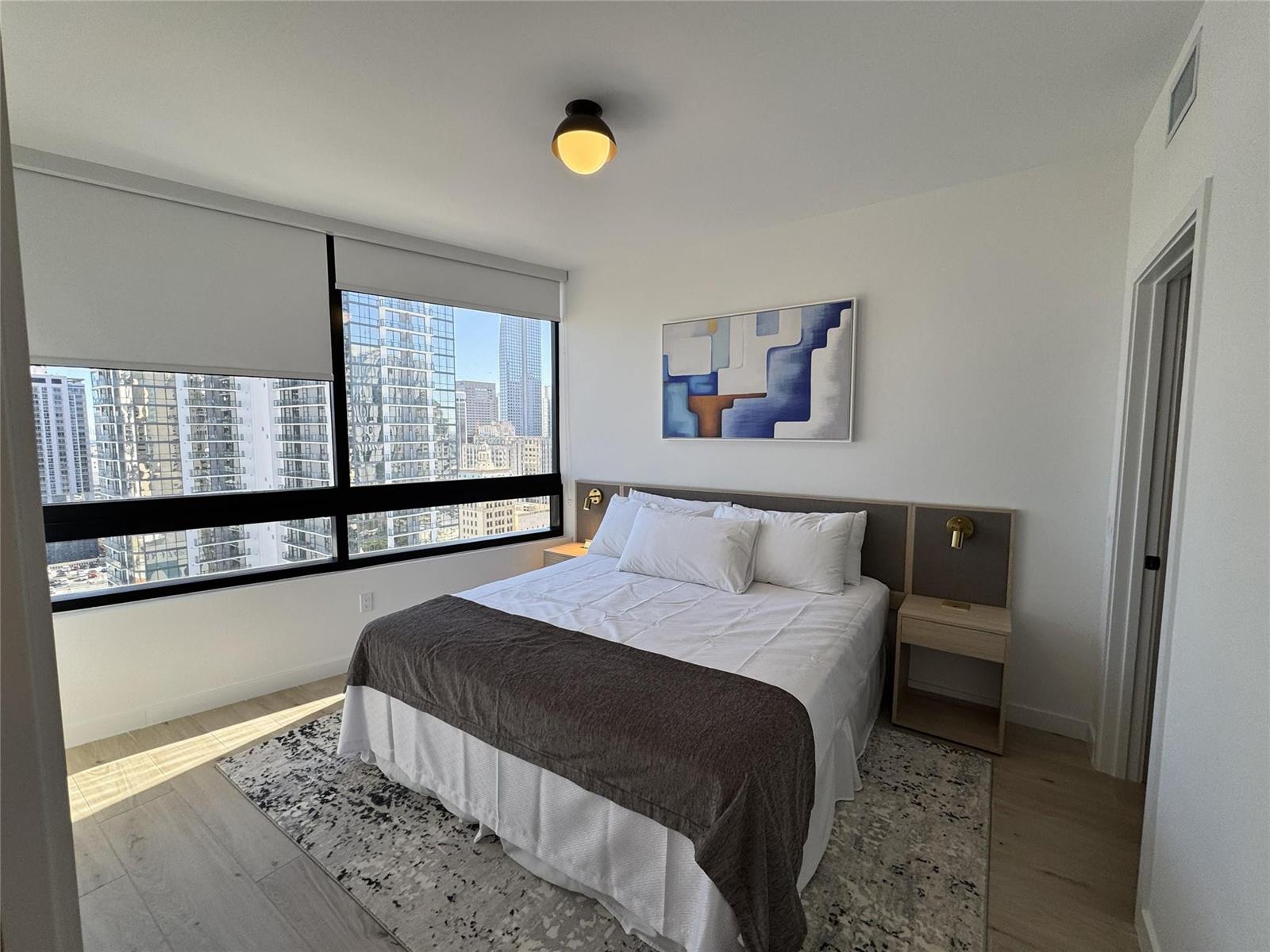 A bedroom features a bed with a dark runner, a patterned rug, and city views — 225 N Miami Avenue # 2507, Miami FL 33128, MIAMI, FL