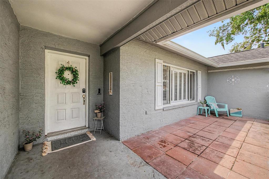 A covered entryway features a white front door, gray stucco walls, and a tiled patio — 2028 NOBLETON AVENUE, SPRING HILL, FL