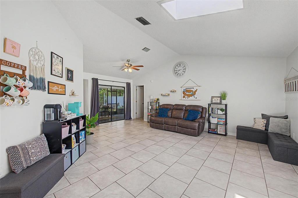 A living room features tile flooring, a vaulted ceiling with a skylight, and a brown sofa — 2028 NOBLETON AVENUE, SPRING HILL, FL