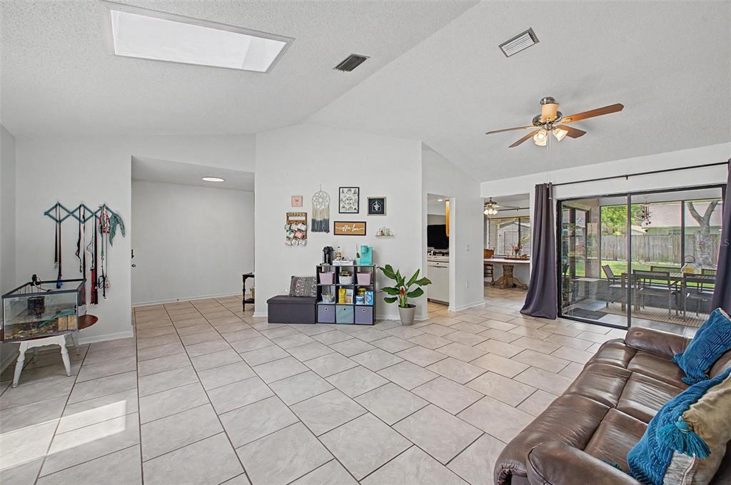 A spacious living room features light tile flooring, a vaulted ceiling, and sliding glass doors — 2028 NOBLETON AVENUE, SPRING HILL, FL