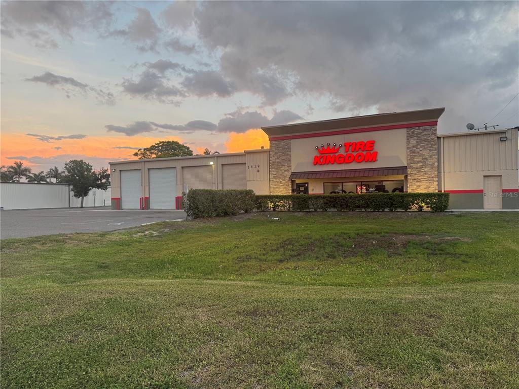 A commercial Tire Kingdom building with multiple garage bays stands behind a grassy lawn — 1429 10TH STREET E, PALMETTO, FL