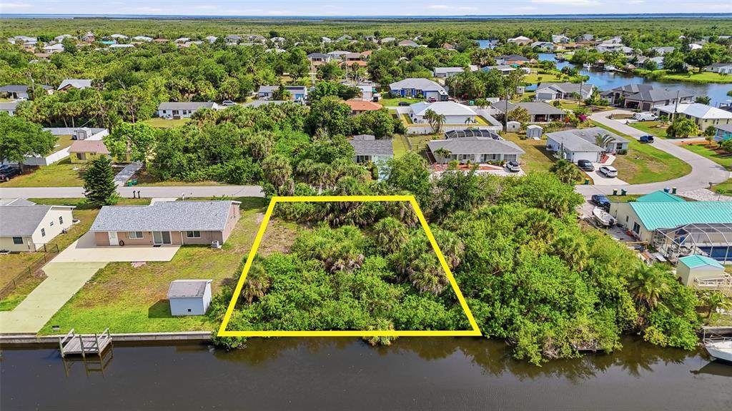 An aerial view shows a vacant, tree-covered waterfront lot outlined in yellow between two houses — 18318 VAN NUYS CIRCLE, PORT CHARLOTTE, FL