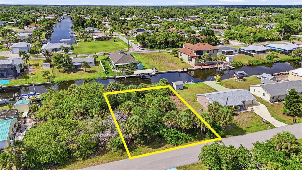 An aerial view shows a vacant, wooded residential lot outlined in yellow along a canal — 18318 VAN NUYS CIRCLE, PORT CHARLOTTE, FL