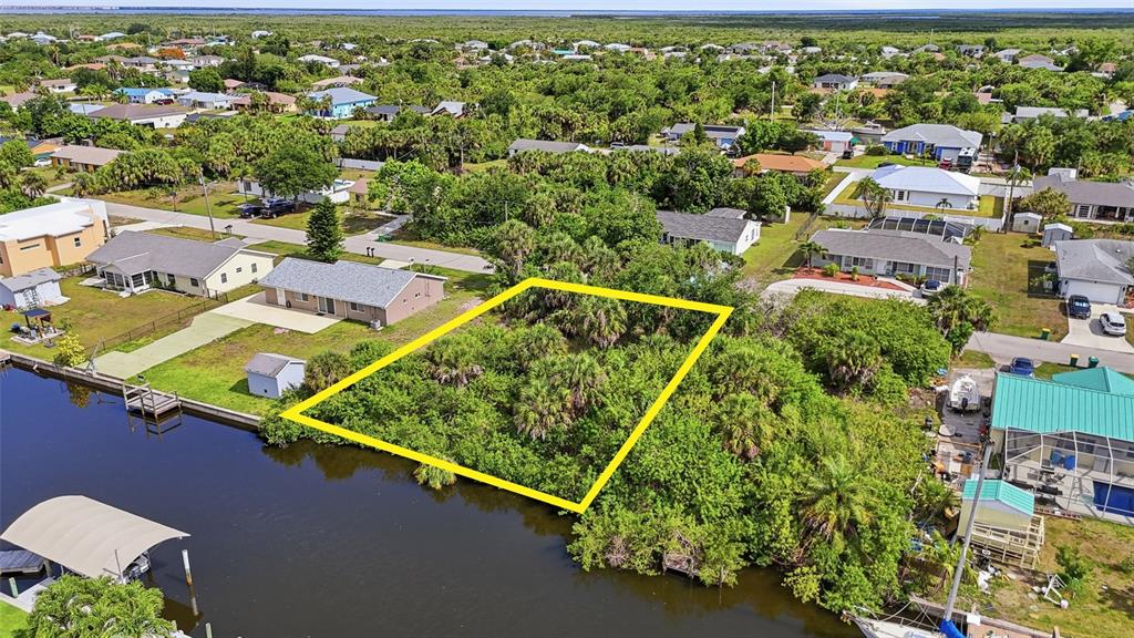 An aerial view shows a vacant, wooded waterfront lot outlined in yellow near residential homes — 18318 VAN NUYS CIRCLE, PORT CHARLOTTE, FL