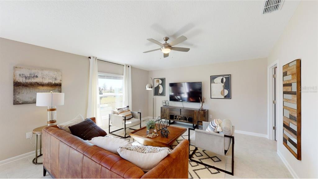 A living room features a leather sofa, two armchairs, a television, and a ceiling fan — 5246 WORCHESTER DRIVE, KISSIMMEE, FL