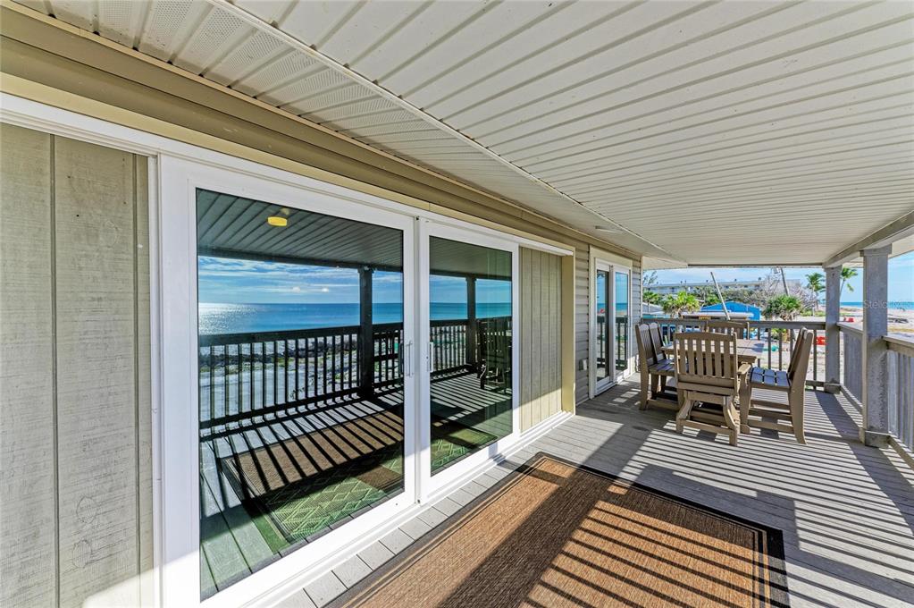A covered wooden deck features a dining set and sliding glass doors overlooking the ocean — 45 WILHELM DRIVE, ENGLEWOOD, FL