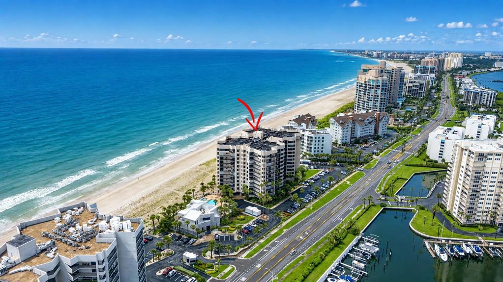 An aerial view shows a beachfront high-rise condominium building next to a road and marina — 1600 GULF BOULEVARD UNIT 911, CLEARWATER BEACH, FL