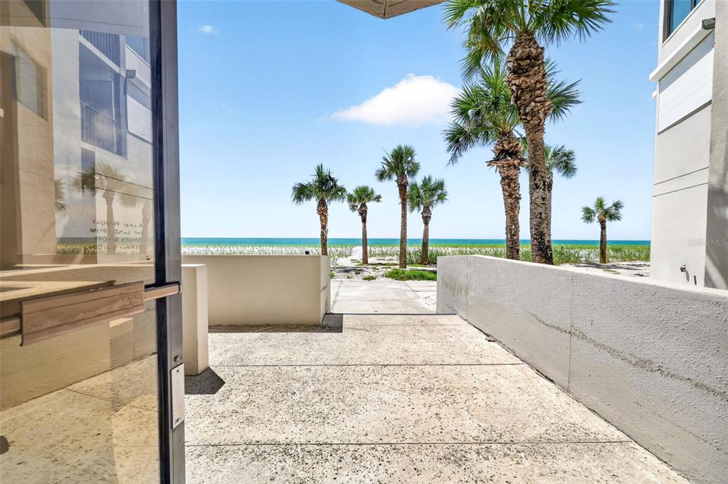 A concrete patio leads to a sandy beach with palm trees and the ocean beyond — 1600 GULF BOULEVARD UNIT 911, CLEARWATER BEACH, FL