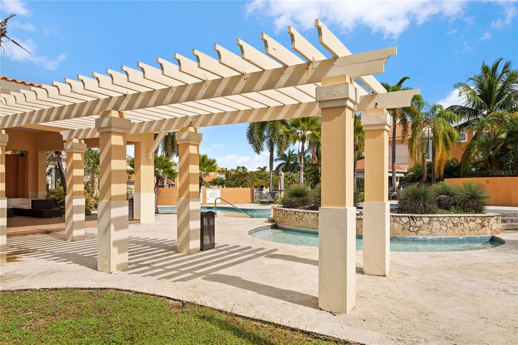 A beige pergola covers a patio area next to a swimming pool and palm trees — 26 FLAMBOYAN GREENS, HUMACAO, PR