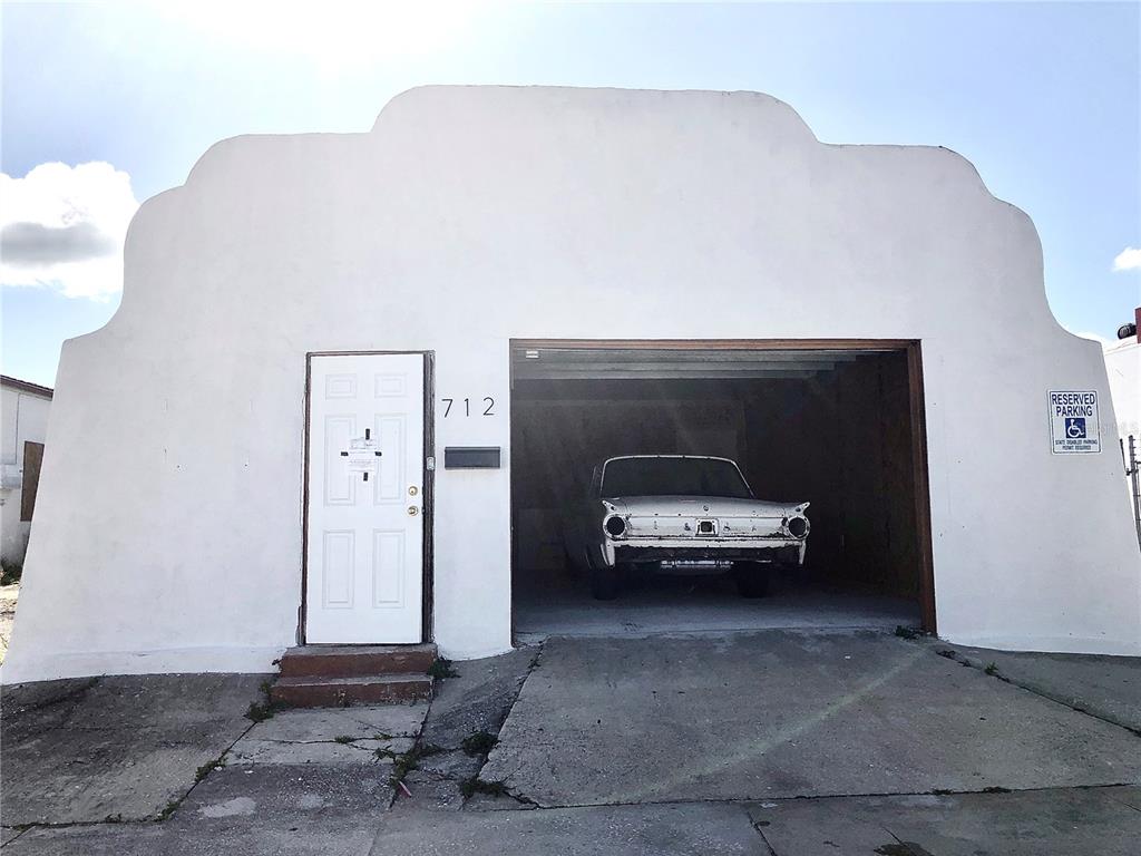 A white building with a mission-style roofline features a single door and an open garage — 712 N RIDGEWOOD DRIVE, SEBRING, FL