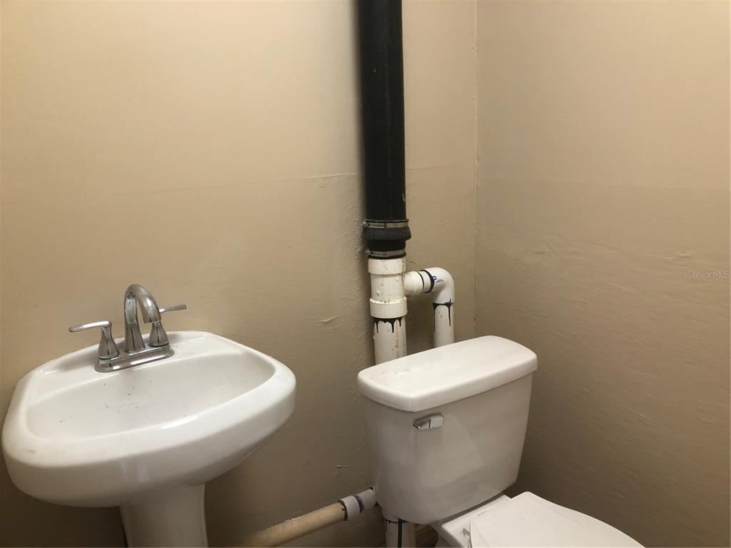 A bathroom features a pedestal sink next to a toilet with exposed plumbing pipes — 712 N RIDGEWOOD DRIVE, SEBRING, FL
