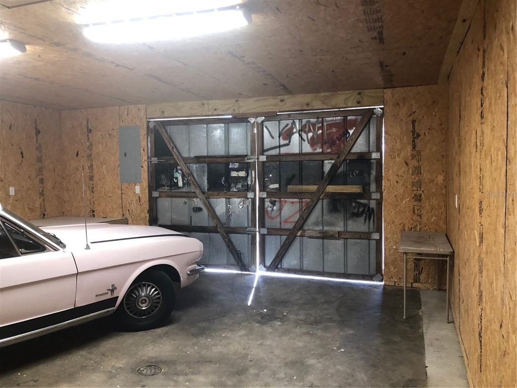 A garage with plywood walls, a concrete floor, and a vintage car parked inside — 712 N RIDGEWOOD DRIVE, SEBRING, FL