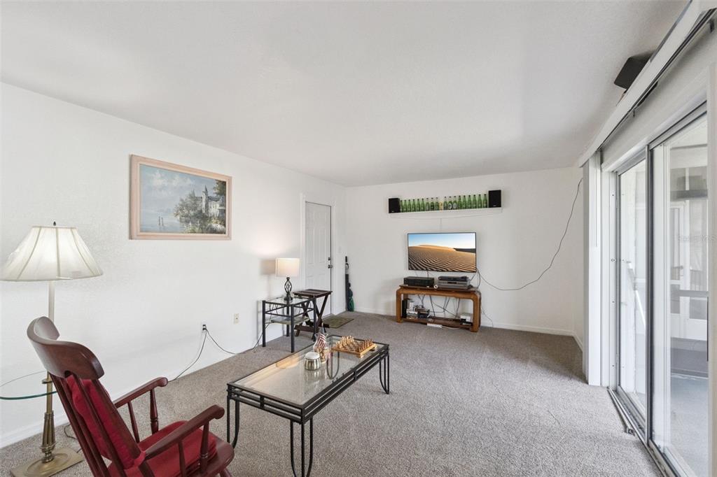 A living room features carpeted flooring, a glass coffee table, a television, and a rocking chair — 1036 PLANTATION DRIVE UNIT D8, KISSIMMEE, FL