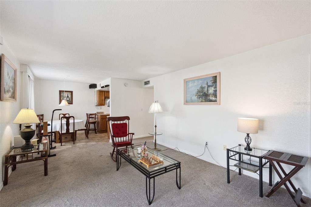 A living room with carpeted floors, a glass coffee table, and an adjacent dining area — 1036 PLANTATION DRIVE UNIT D8, KISSIMMEE, FL