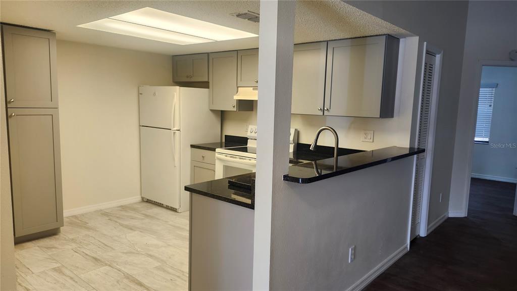 A kitchen features gray cabinets, black countertops, a white refrigerator, and light-colored tile flooring — 7413 MEAD DRIVE, SPRING HILL, FL