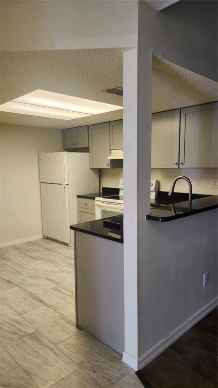 A kitchen features grey cabinets, black countertops, a white refrigerator, and light-colored tile flooring — 7413 MEAD DRIVE, SPRING HILL, FL