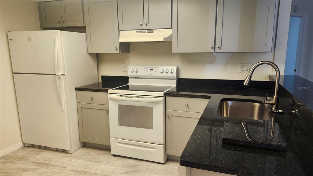 A kitchen features gray cabinets, black countertops, a white stove, and a white refrigerator — 7413 MEAD DRIVE, SPRING HILL, FL