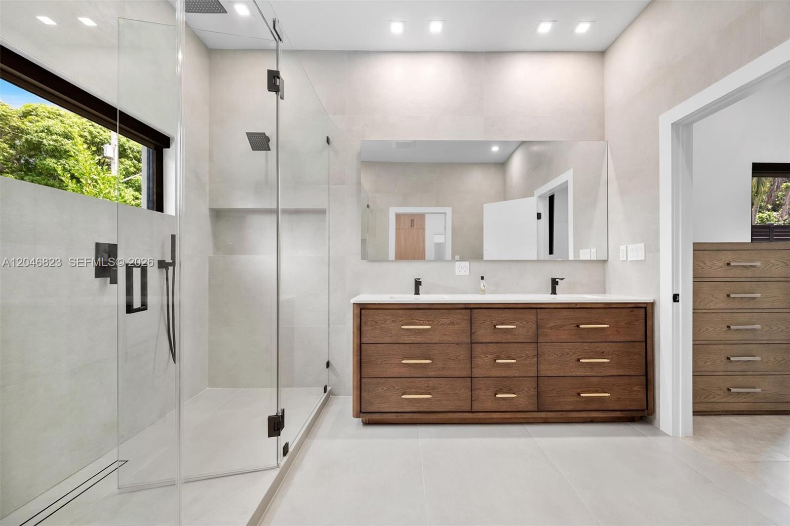 A modern bathroom features a glass-enclosed shower, a double-sink vanity, and light-colored tile walls — 95 NW 52nd St, Miami FL 33127, MIAMI, FL