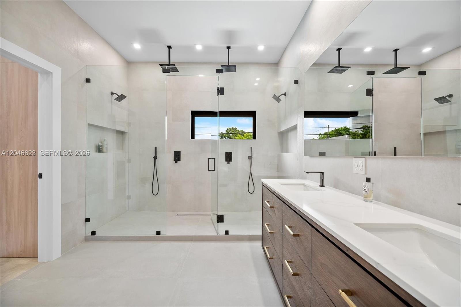 A modern bathroom features a double walk-in shower with glass doors and a wood vanity — 95 NW 52nd St, Miami FL 33127, MIAMI, FL