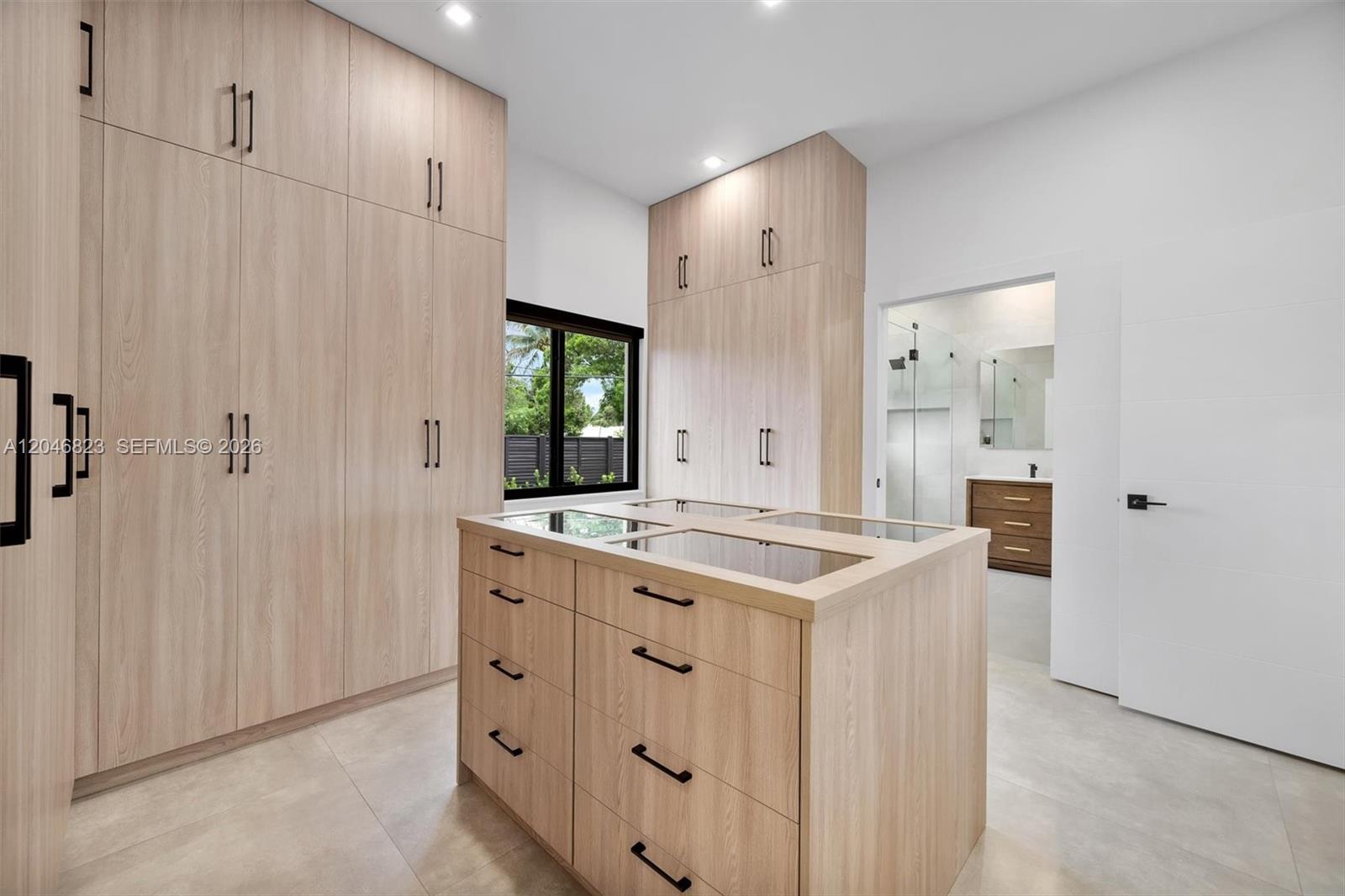 A walk-in closet features light wood cabinetry, a central island with glass-top drawers, and tile flooring — 95 NW 52nd St, Miami FL 33127, MIAMI, FL