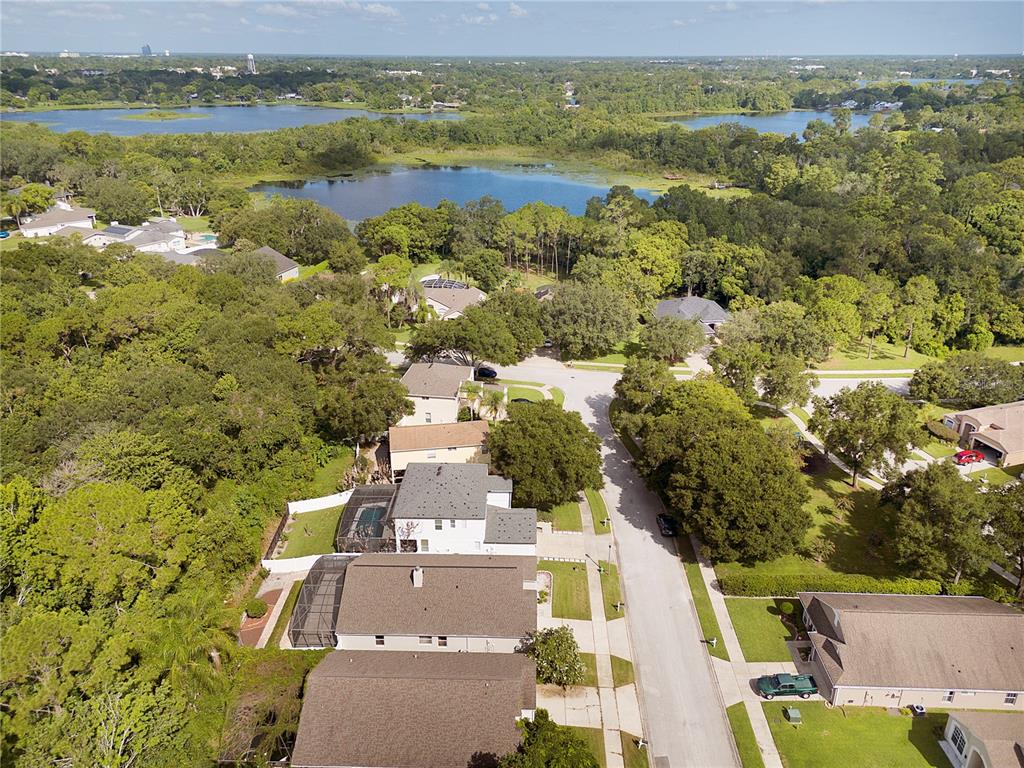 An aerial view shows suburban houses surrounded by dense trees and nearby lakes — 839 MATTOCKS COURT, CASSELBERRY, FL