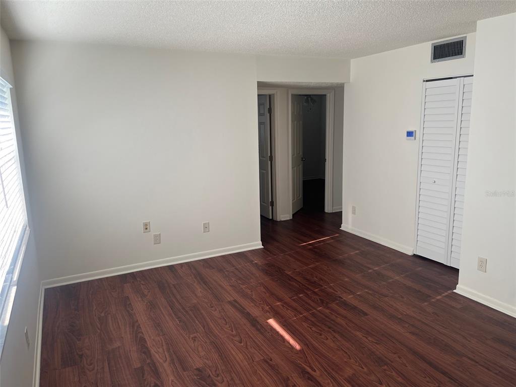 An empty room features wood-look flooring, white walls, a louvered closet door, and two doorways — 105 11TH AVENUE UNIT 10, ST PETE BEACH, FL
