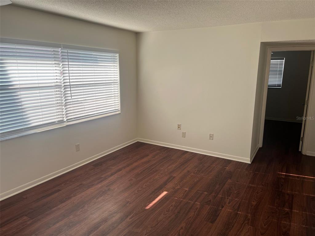 An empty room with dark wood-look flooring, white walls, and a window with blinds — 105 11TH AVENUE UNIT 10, ST PETE BEACH, FL