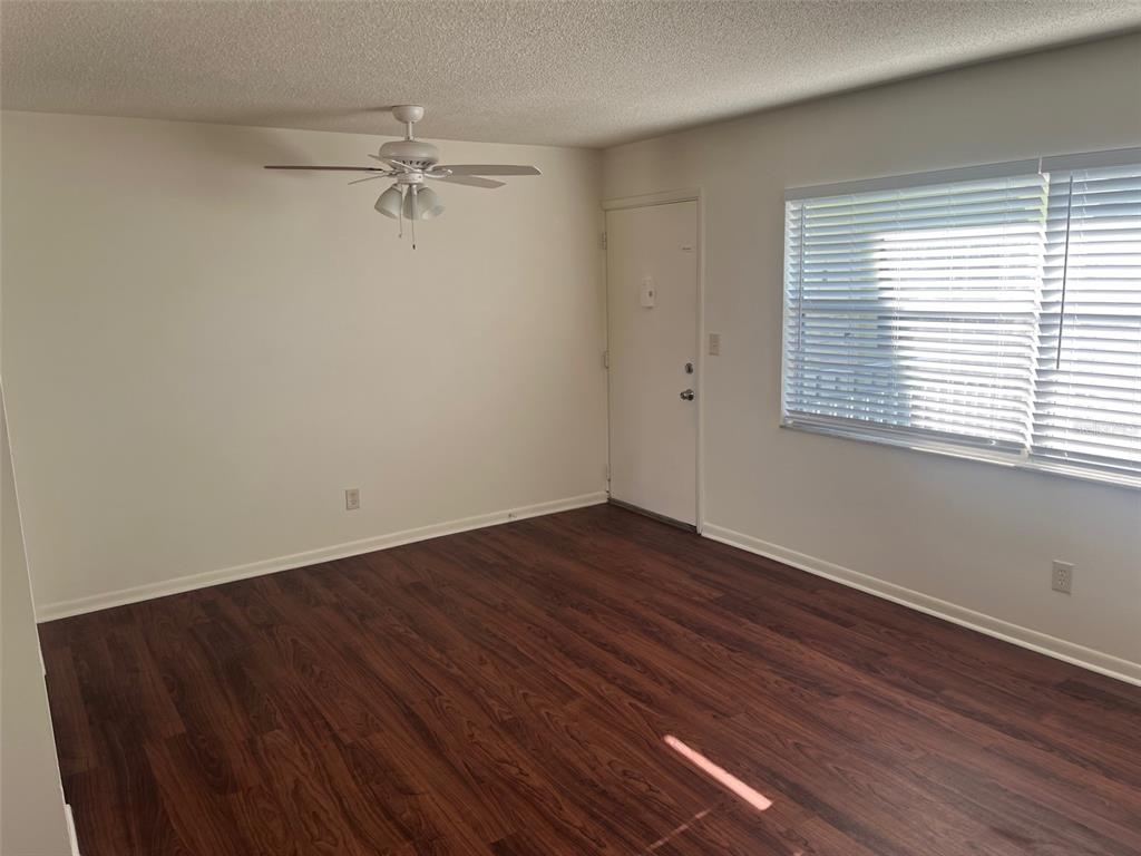 An empty room features dark wood-look flooring, white walls, a ceiling fan, and a window — 105 11TH AVENUE UNIT 10, ST PETE BEACH, FL