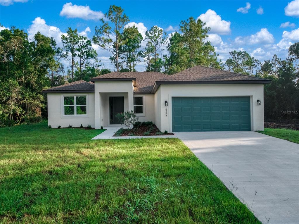 A single-story house with a white stucco exterior, a dark green garage door, and a driveway — 8381 MANTUA AVENUE, SEBRING, FL